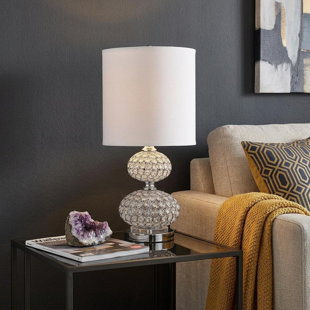 24" Chrome and Faux Crystal Double Orb Table Lamp With White Classic Drum Shade displayed on a tabletop in a furnished interior against a dark wall.