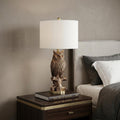 28” Antiqued Silver Resin Owl Table or Desk Lamp styled in a furnished interior with a tan wall on a black floor.