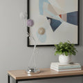 28" Clear Three Light Bedside Led Table Lamp displayed on a wood tabletop in a furnished interior against a light gray wall.