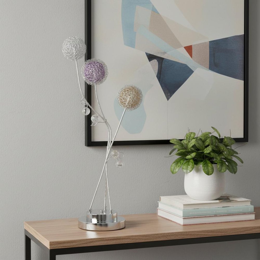 28" Clear Three Light Bedside Led Table Lamp displayed on a wood tabletop in a furnished interior against a light gray wall.
