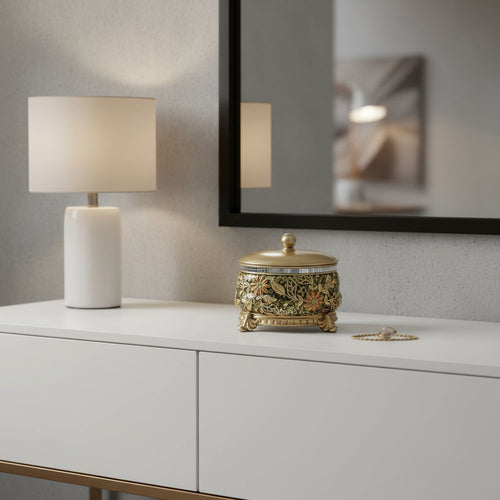 Gold and green resin jewelry box with floral scroll design and metal accents on a white dresser with a lamp and mirror.