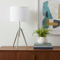 34" Silver Metal Adjustable Tripod Table Lamp With White Round Shade displayed on a dark wood tabletop in a furnished interior against an off-white wall.