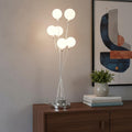 28" Silver Chrome Six Light Globe Desk or Table Lamp displayed on a dark wood tabletop in a furnished interior against a tan wall.