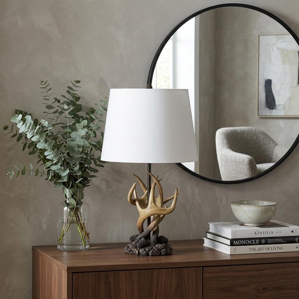 26" Natural And Brown Antlers Table Lamp With White Shade displayed on a dark wood tabletop in a furnished interior against a gray wall.