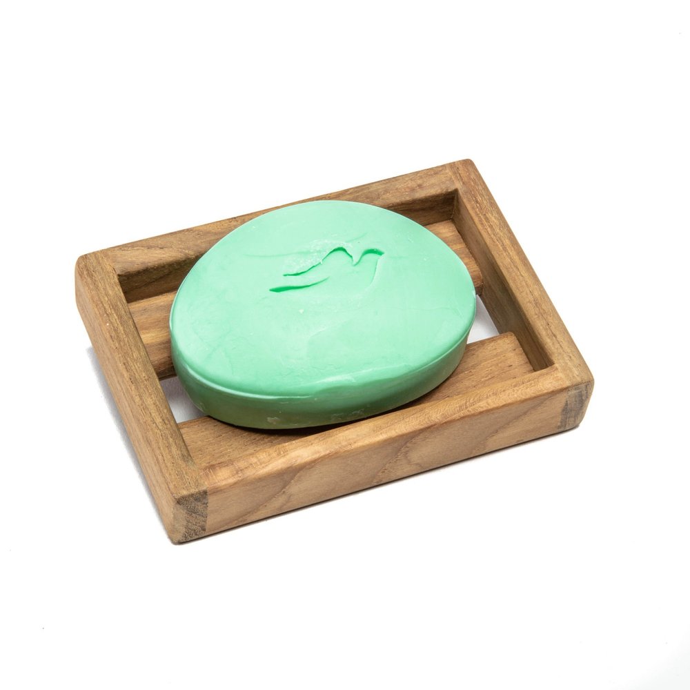 A green bar of soap with a dove logo sits in a wooden soap dish on a white background.