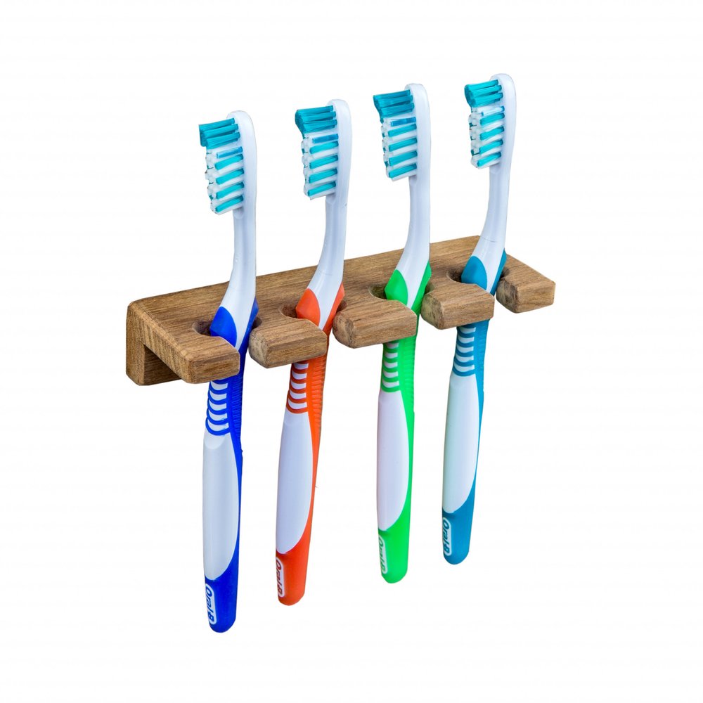 Wooden toothbrush holder with four toothbrushes in blue, orange, green, and blue on a white background.