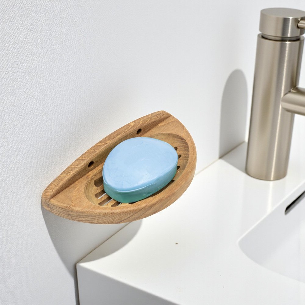 Solid teak wall-mount oval soap dish with a blue bar of soap on a white sink with a brushed nickel faucet.
