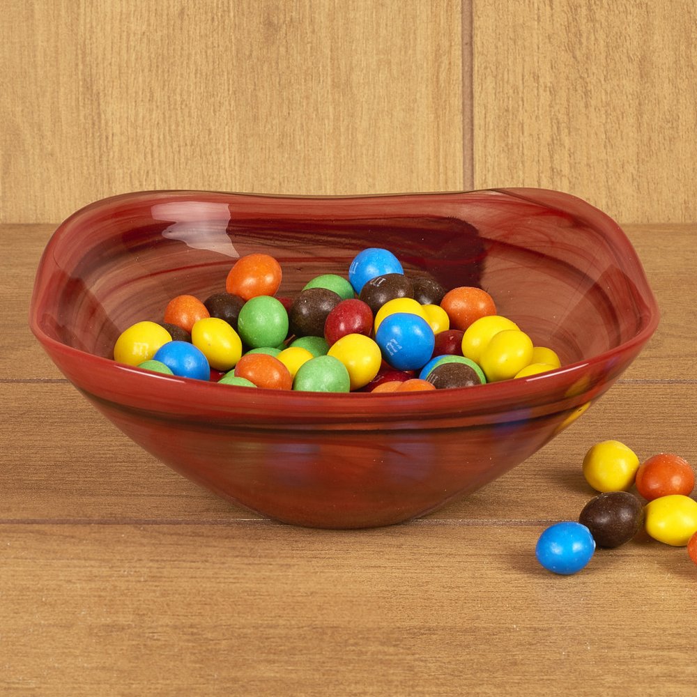 Red swirl glass bowl filled with colorful M&Ms on a wooden surface.