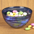 Cobalt and white alabaster glass round candy or nut bowl filled with pastel-colored candies on a wooden surface.