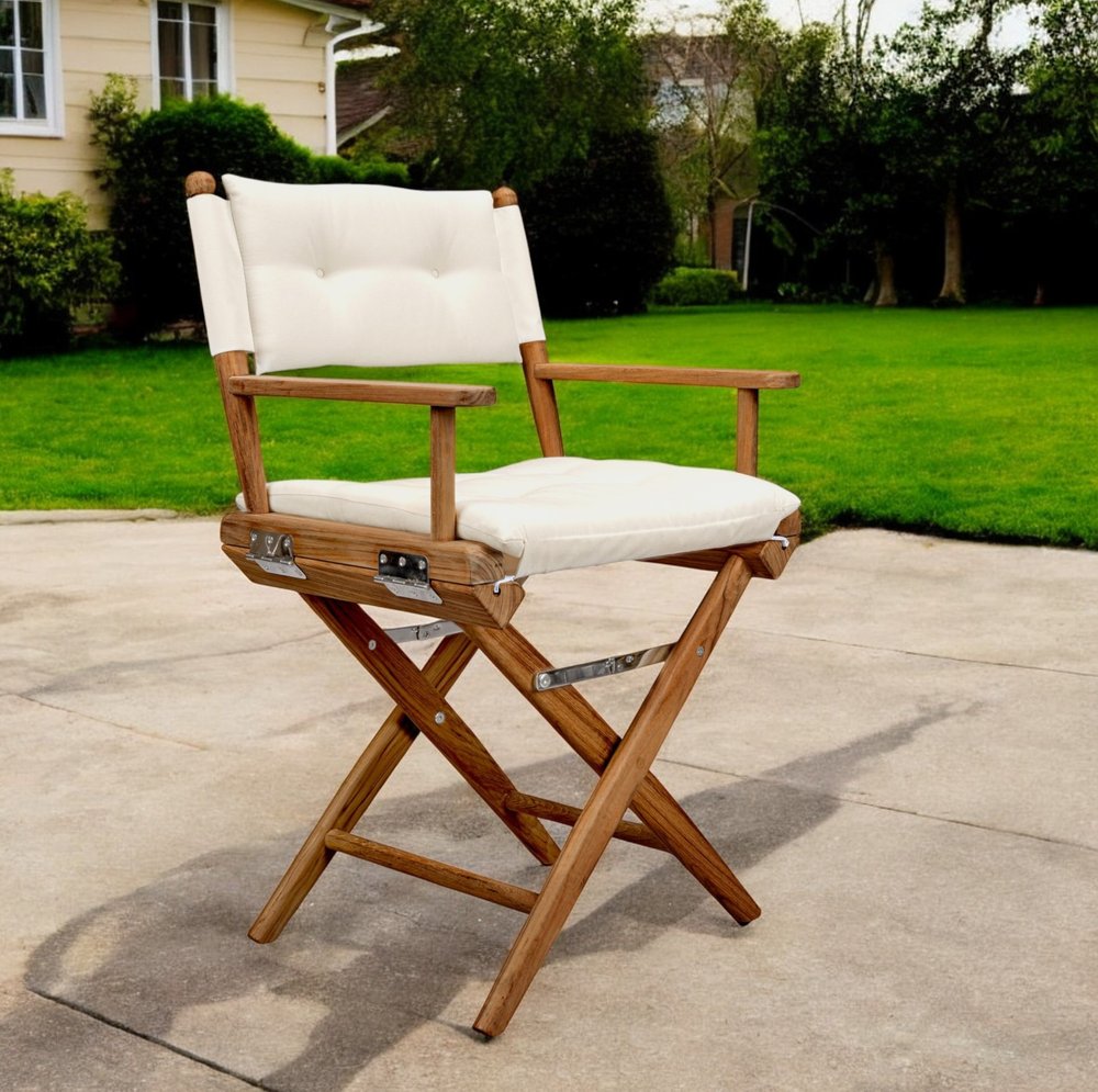 23" Natural Solid Wood Outdoor Folding Director Chair with Cream Cushion shown outdoors on a patio with greenery in ivory wood.