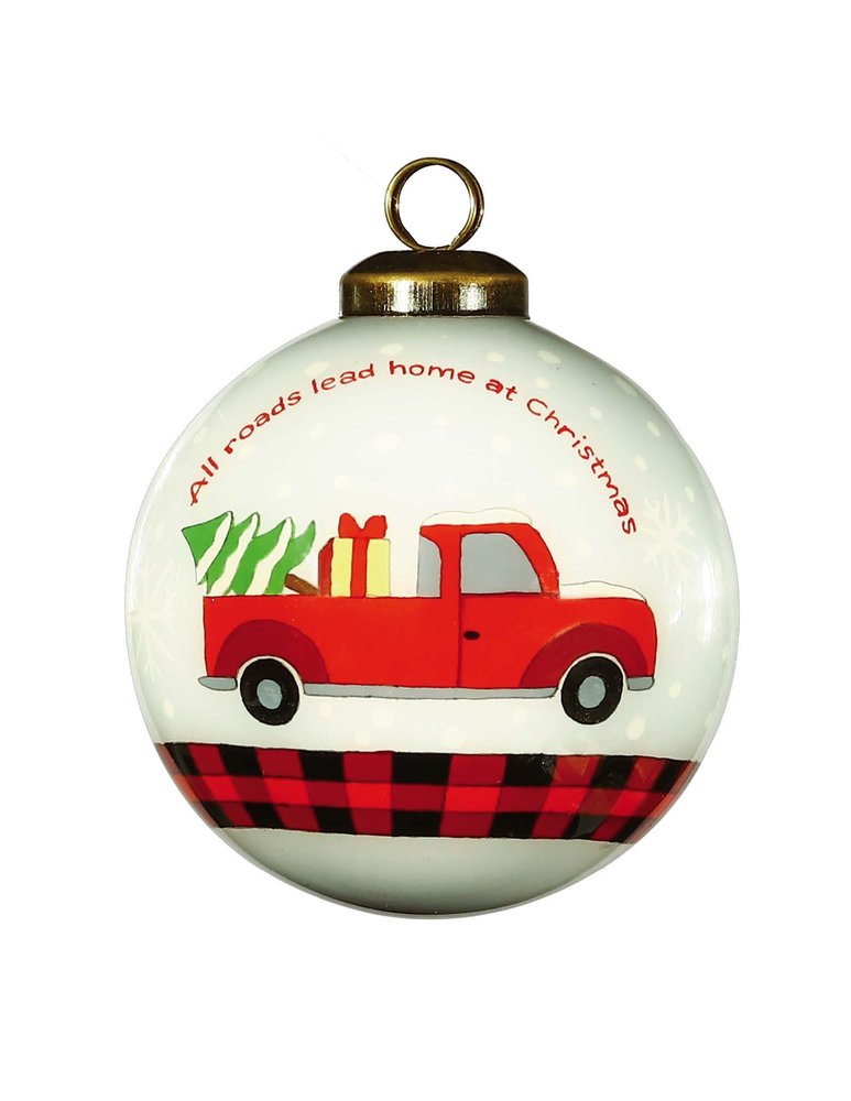 A round white glass Christmas ornament with a red truck carrying a Christmas tree and gifts, with a buffalo plaid border.