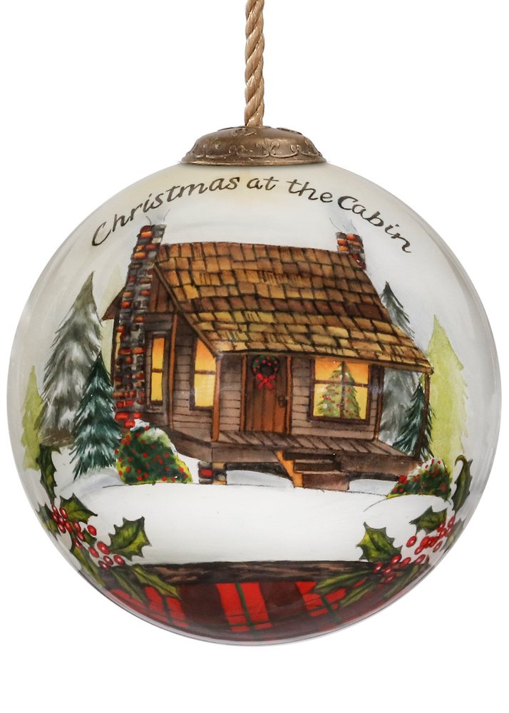 Clear glass Christmas ornament with a hand-painted scene of a snow-covered cabin, trees, and holly.