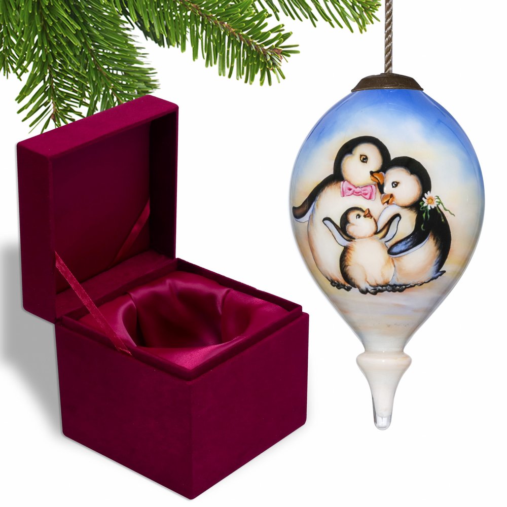 Glass finial ornament with a penguin family painted on it, next to an open velvet gift box.
