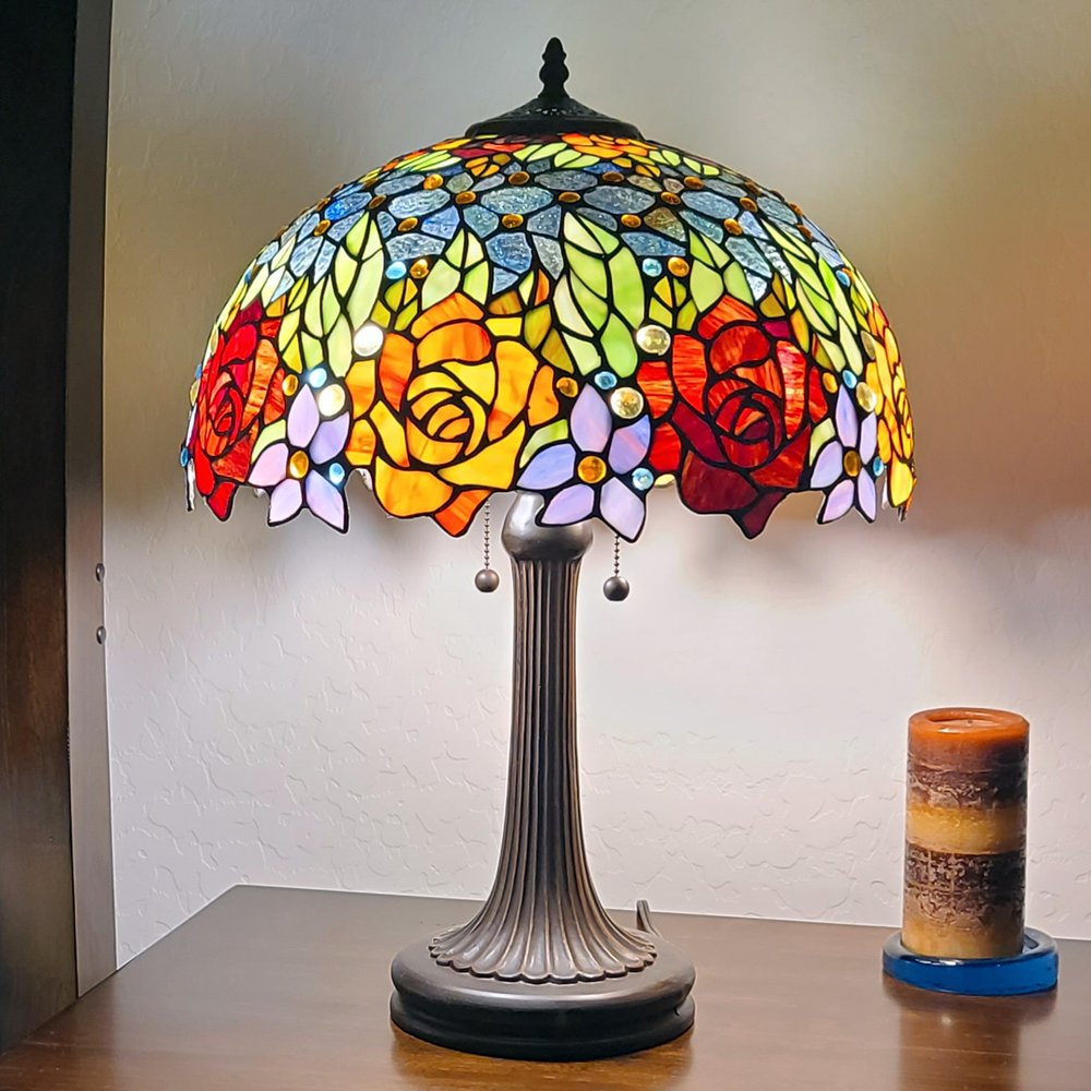 24" Dark Brown Metal Two Light Candlestick Table Lamp With Orange Shade displayed on a wood tabletop in a furnished interior against a tan wall.
