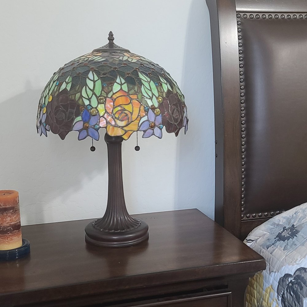24" Dark Brown Metal Two Light Candlestick Table Lamp With Orange Shade displayed on a tabletop in a furnished interior against an off-white wall.