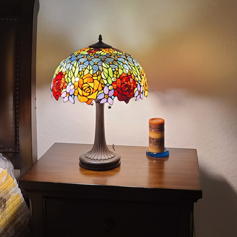 24" Dark Brown Metal Two Light Candlestick Table Lamp With Orange Shade displayed on a tabletop in a furnished interior against a tan wall.