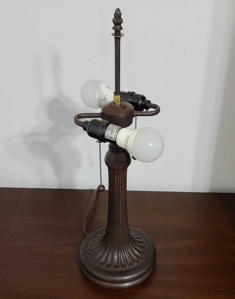 24" Dark Brown Metal Two Light Candlestick Table Lamp With Dark Brown Shade displayed on a dark wood tabletop in a furnished interior against an off-white wall.