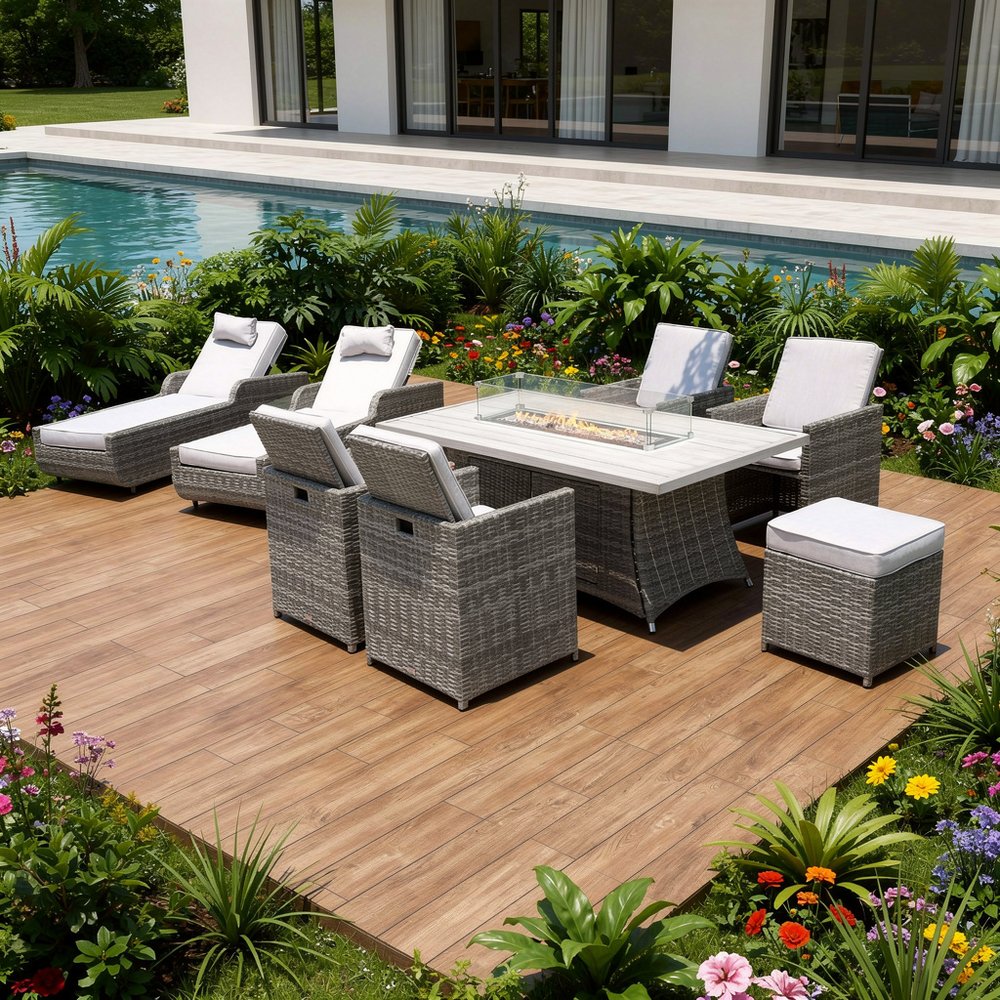 Gray wicker outdoor seating group with multiple chairs, a fire pit table, and gray cushions on a wooden deck with a pool and garden.