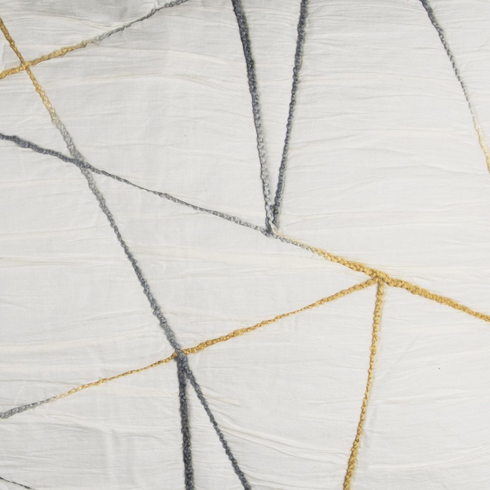 Close-up of a king quilt with an abstract pattern of gray and gold stitched lines on an ivory textured background.