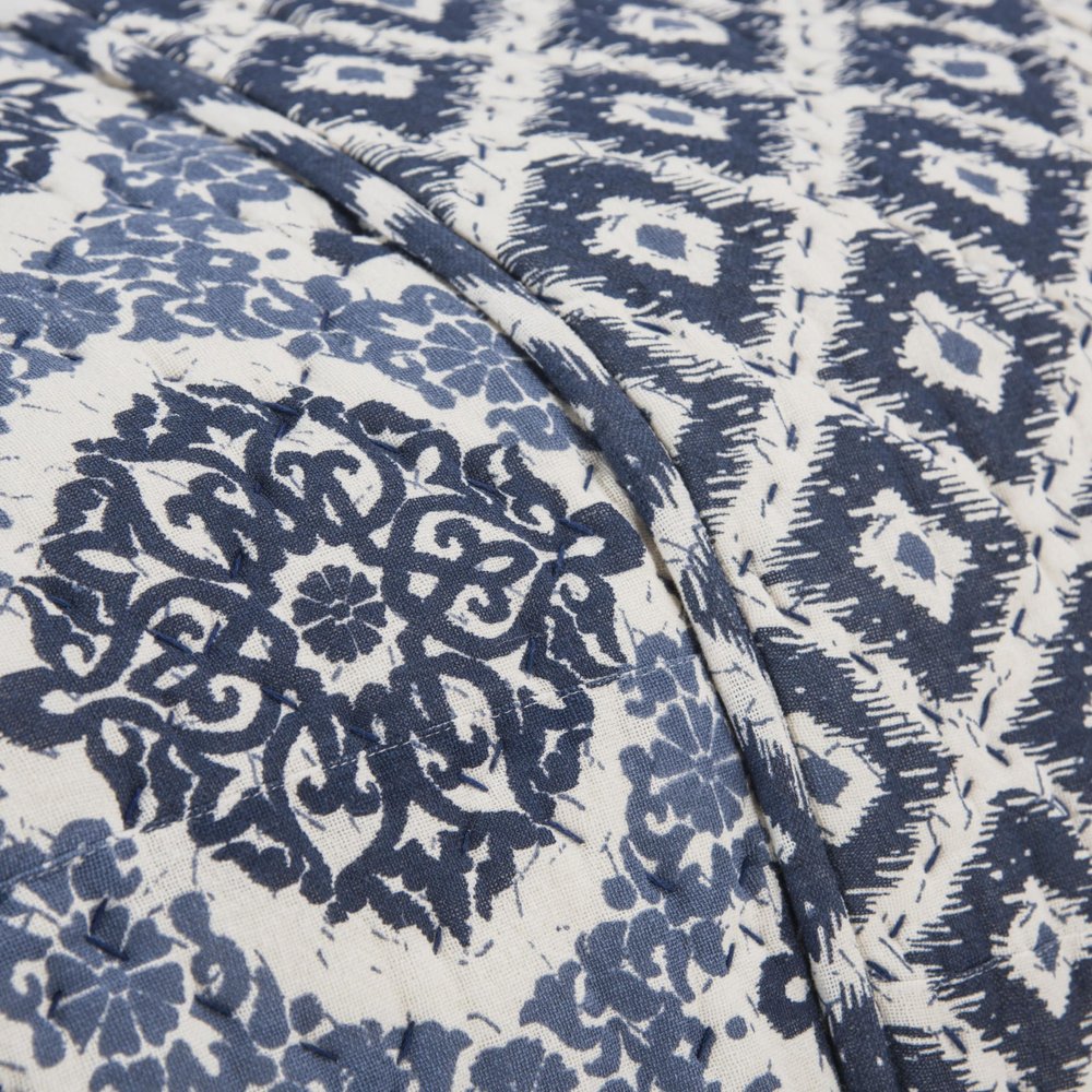 Close-up of a blue and ivory damask queen quilt with a textured fabric and quilted stitching.