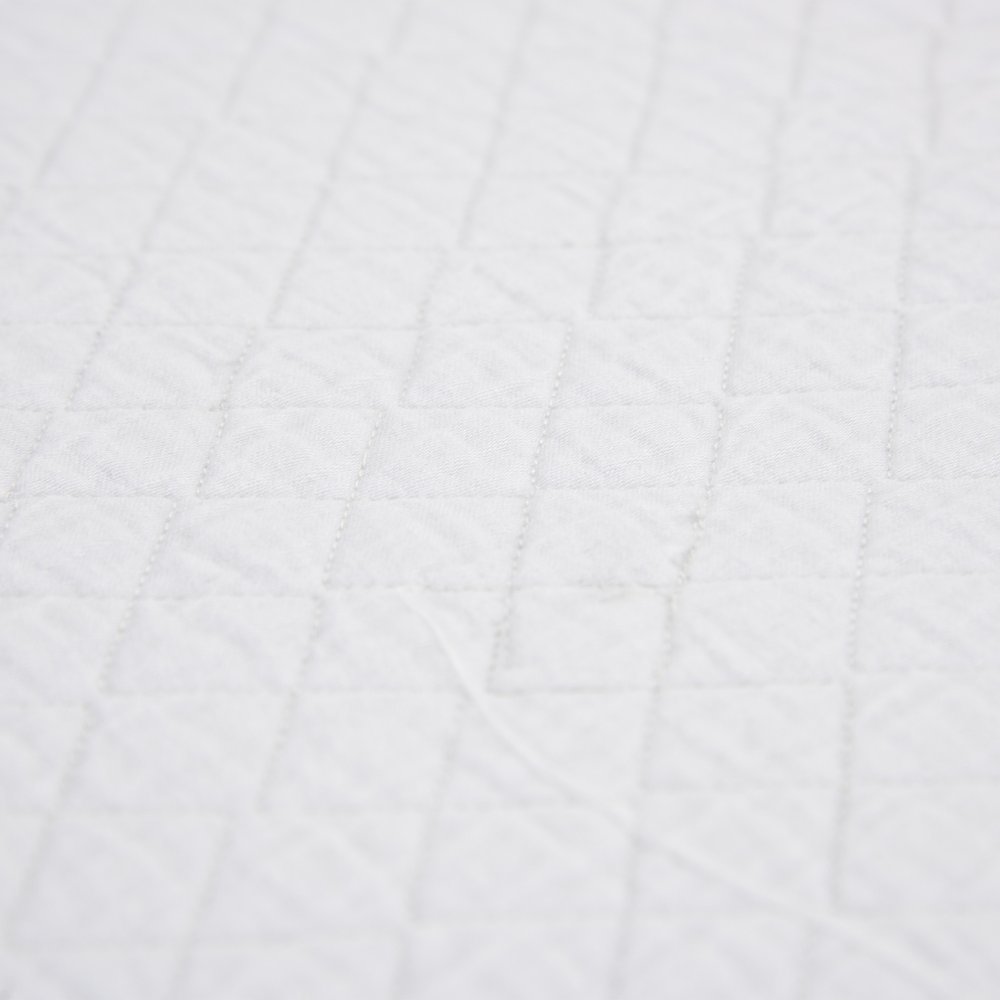 Close-up of a white checkered king quilt, showing the diamond pattern stitching on a soft fabric.
