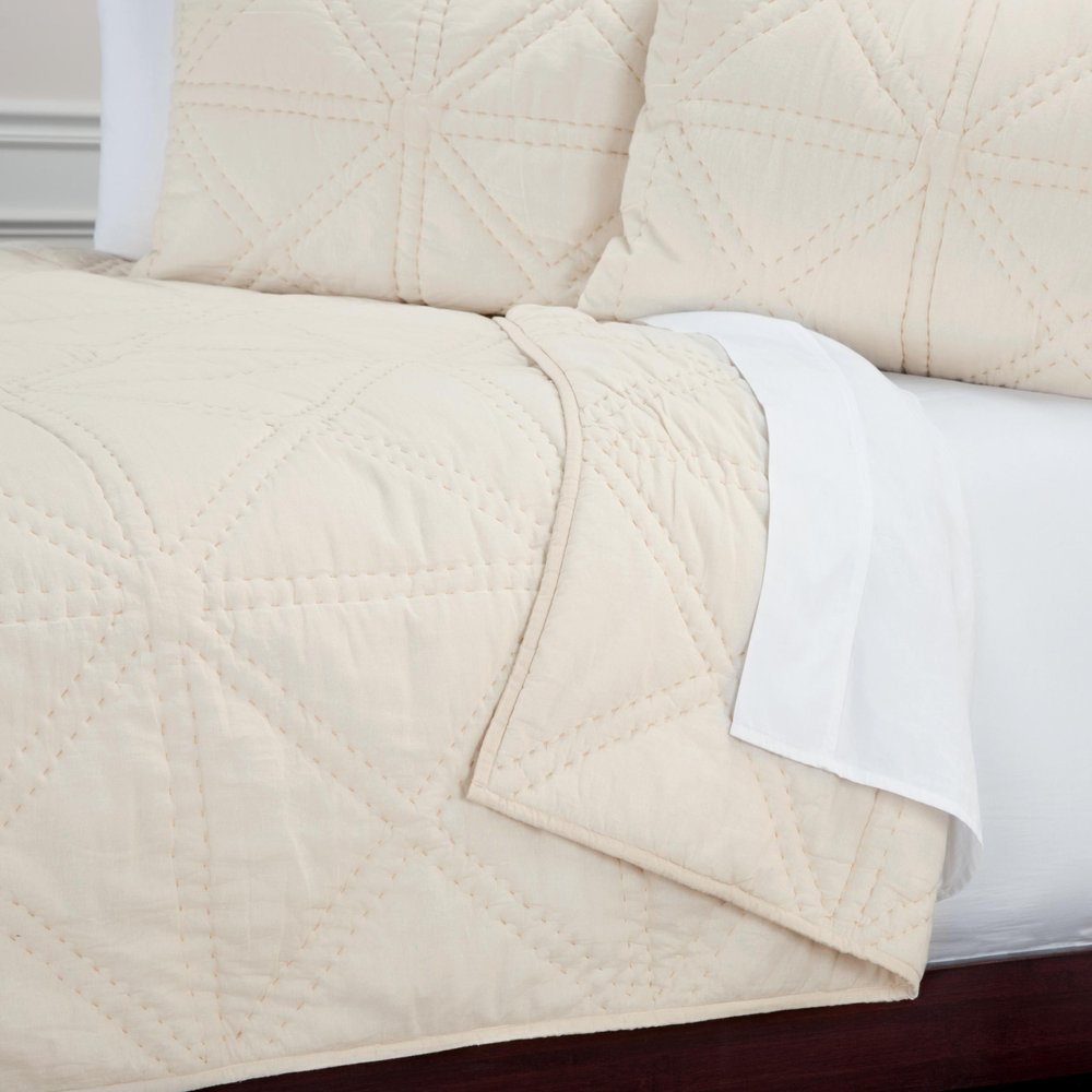 Ivory geometric quilted queen quilt and pillows on a bed with white sheets.