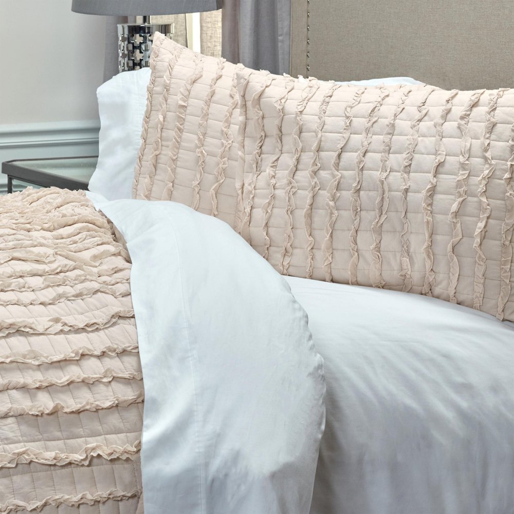 Close-up of a blush pink queen quilt with ruffled stripes and white bedding on a bed.