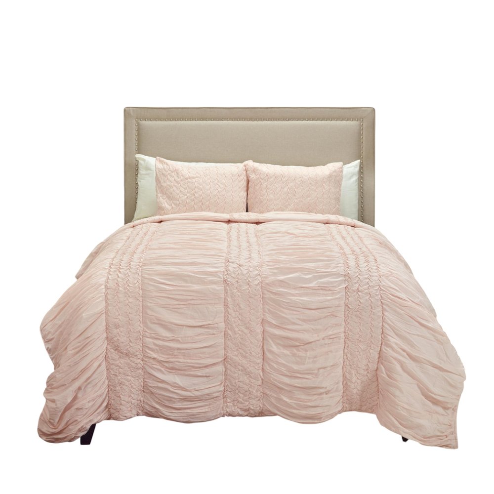 Pink geometric king quilt on a bed with a beige upholstered headboard against a white background.