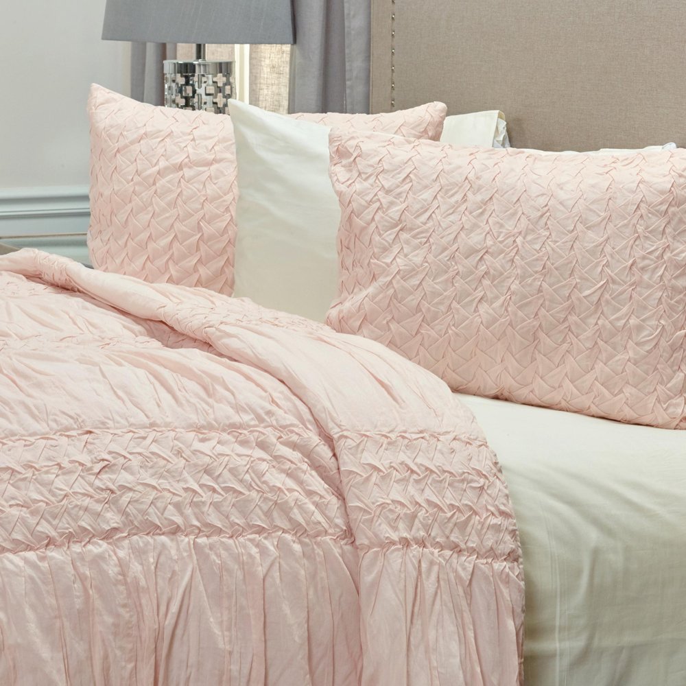 Close-up of a pink geometric queen quilt and pillows on a bed with a beige headboard and gray curtains.