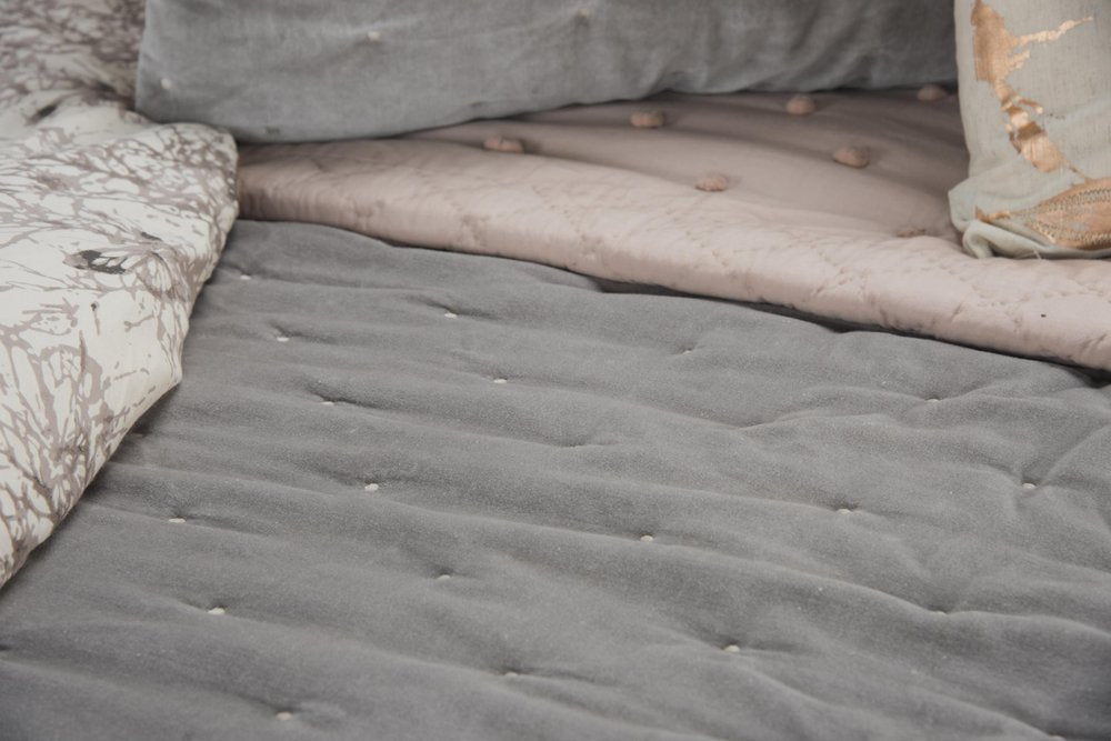 Close-up of a gray quilted bedspread with white polka dots, layered with a pink quilt and a patterned throw.
