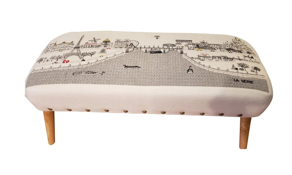 Cream wool ottoman with a black and white Paris street scene print and four wooden legs.
