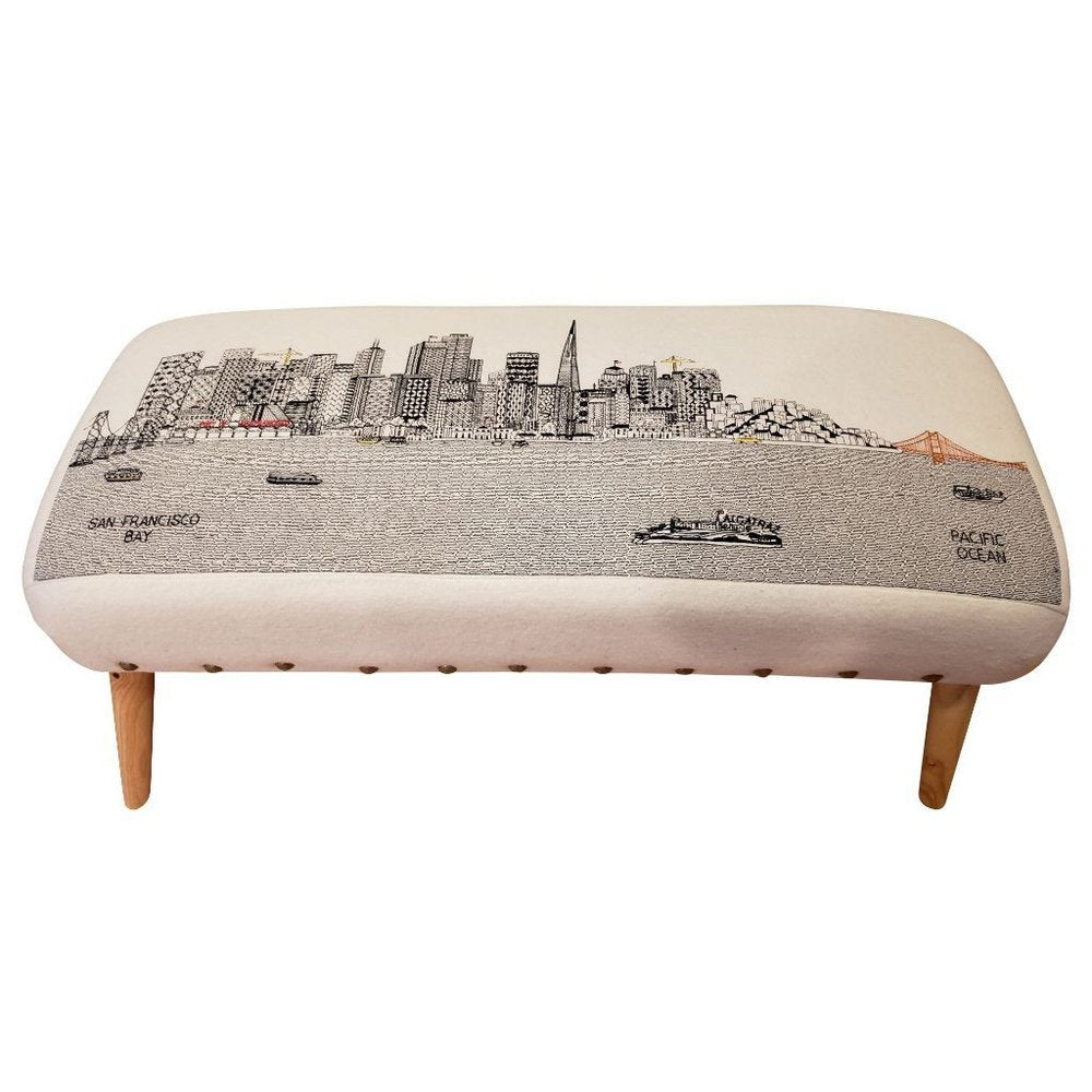Cream wool ottoman with a black and white San Francisco skyline embroidered design and wooden legs.