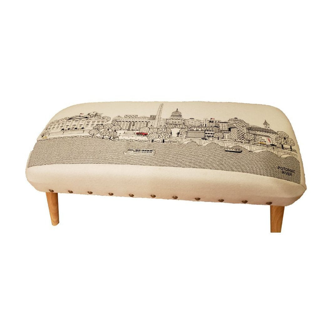Cream wool ottoman with a black and white Washington D.C. skyline print and four wooden legs.