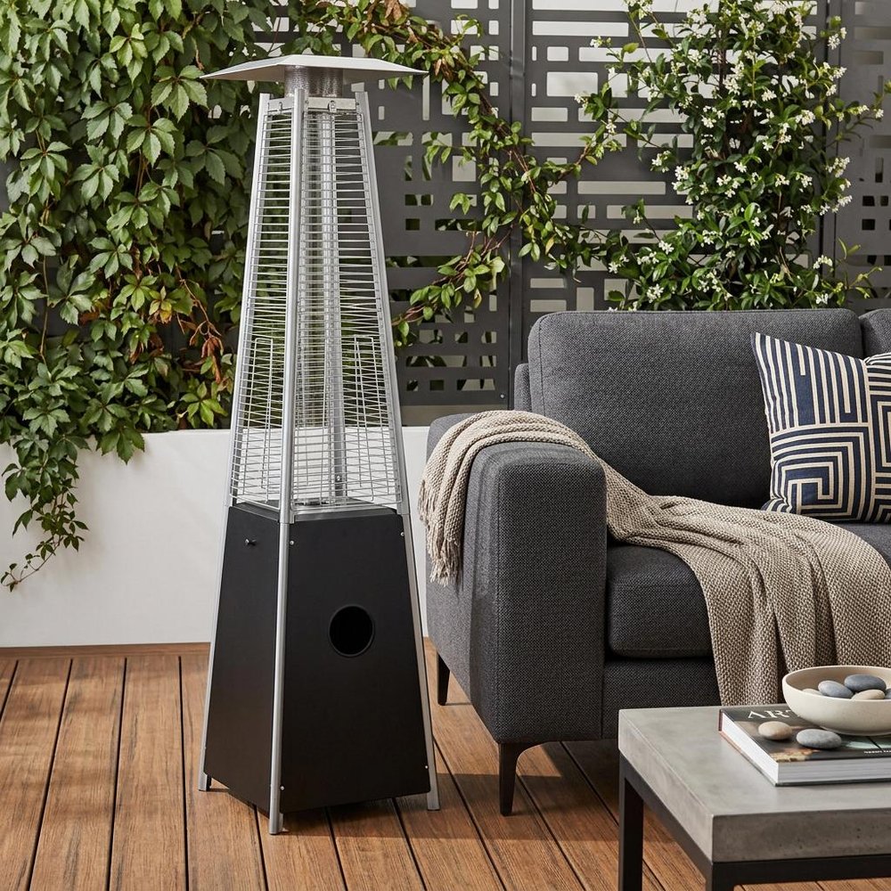 41000 BTU Black Steel Propane Triangular Pyramid Standing Patio Heater styled in a furnished interior with a olive wall on a wood floor.