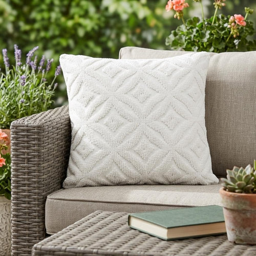 White textured ogee decorative pillow on an outdoor sofa with plants and a book on a table.