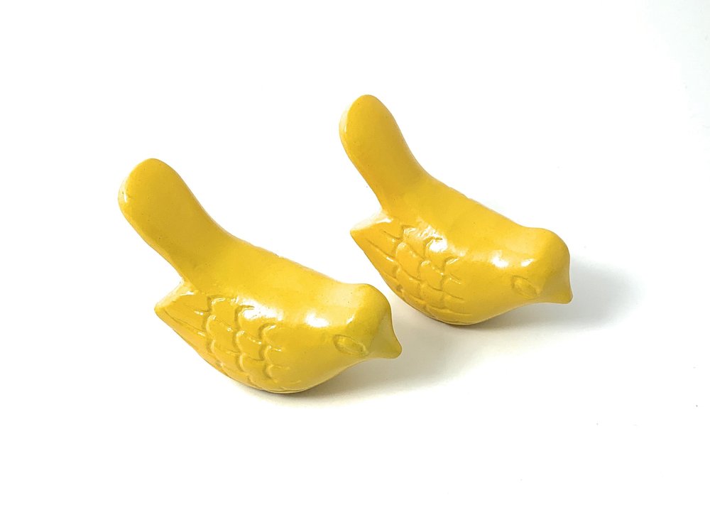 Two yellow metal bird sculptures on a white background.