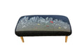Black embroidered ottoman with a Boston night skyline and Charles River scene, featuring wooden legs.
