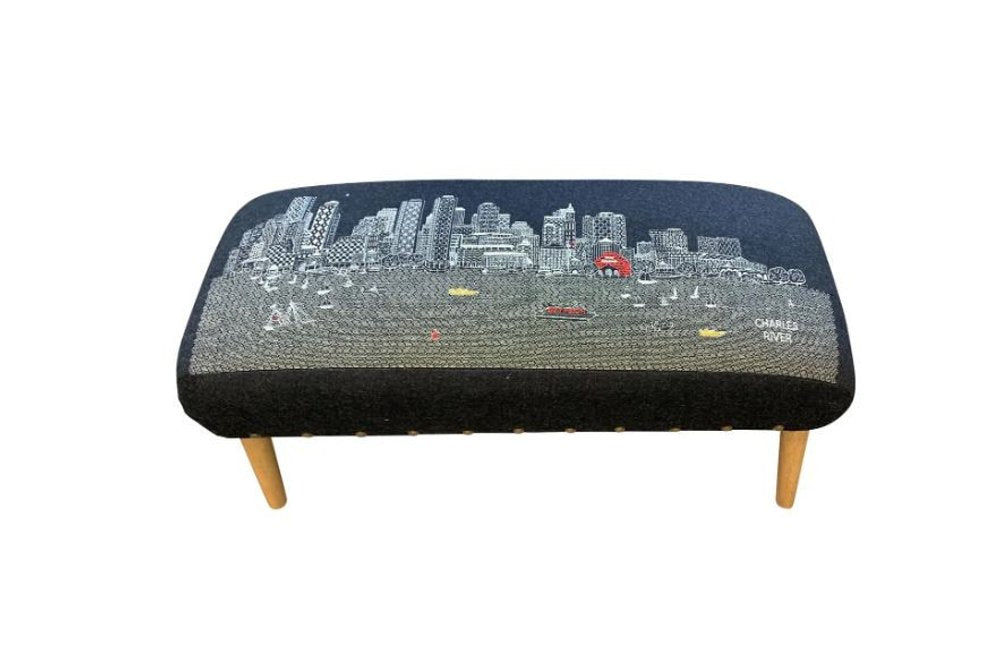 Black embroidered ottoman with a Boston night skyline and Charles River scene, featuring wooden legs.