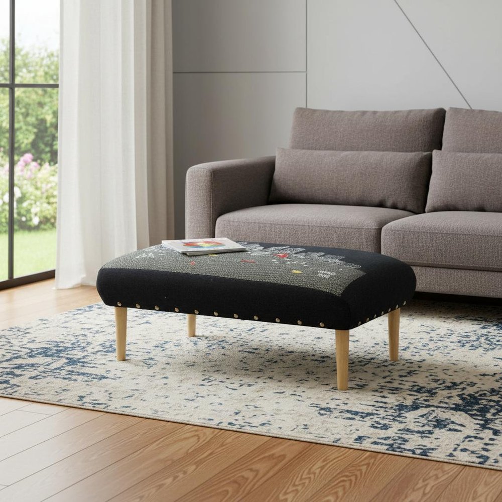 38" Black And Natural Boston Night Skyline Embroidered Ottoman styled in a furnished interior with a light gray wall on a dark wood floor.