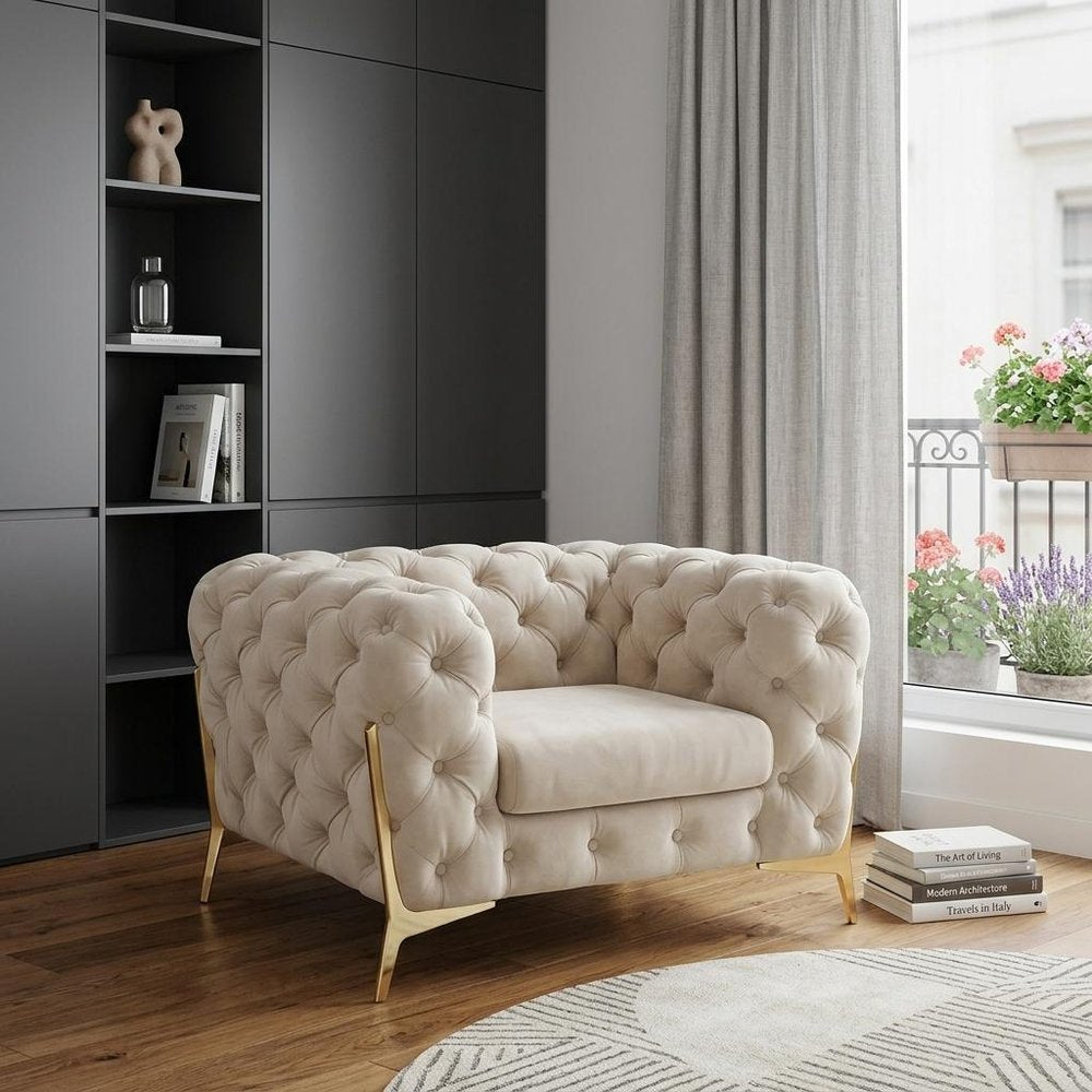 50" Beige And Gold Velvet Tufted Lounge Chair styled in a furnished interior on a dark wood floor against a gray wall.