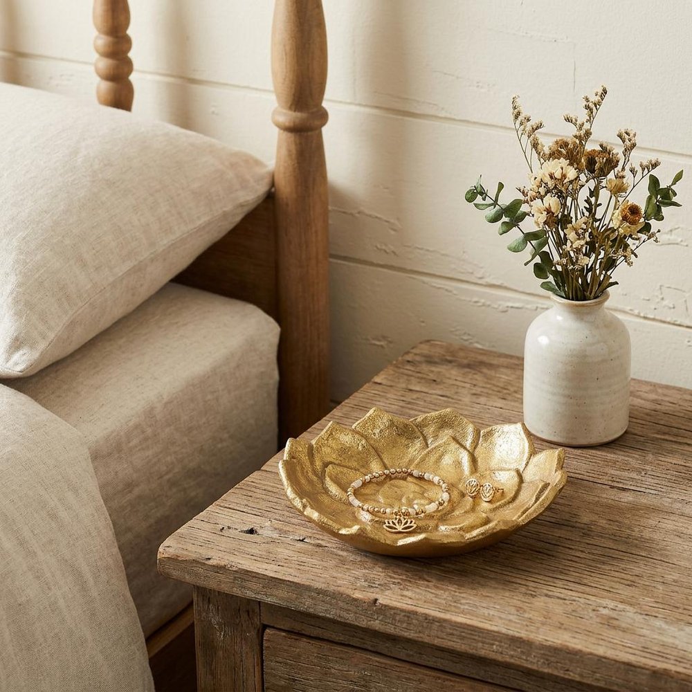 6" Gold Lotus Flower Metal Lotus Leaf Handmade Vanity Tray styled in a furnished interior with an off-white wall on a dark wood floor.