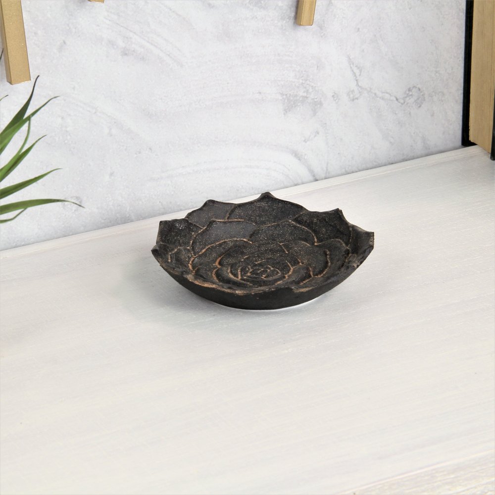 Black metal tray with a rose design on a white wooden surface with a textured gray wall in the background.