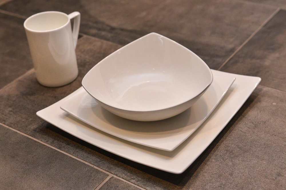 White bone china dinnerware set with a mug, bowl, and plates stacked on a dark tiled surface.