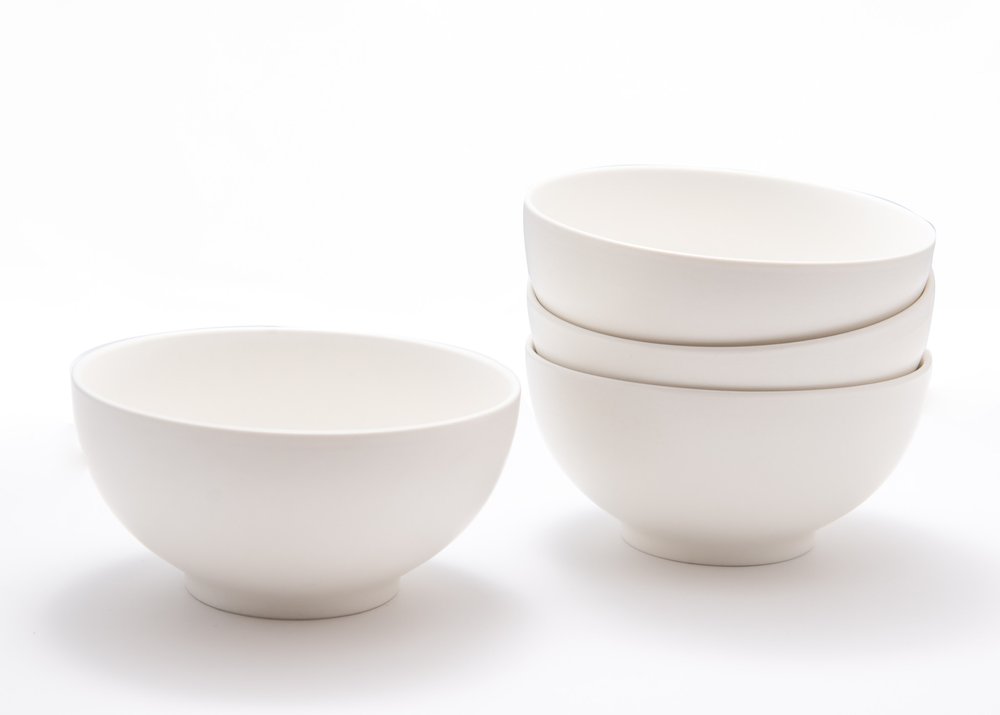 Four white porcelain bowls stacked and one bowl to the left on a white background.
