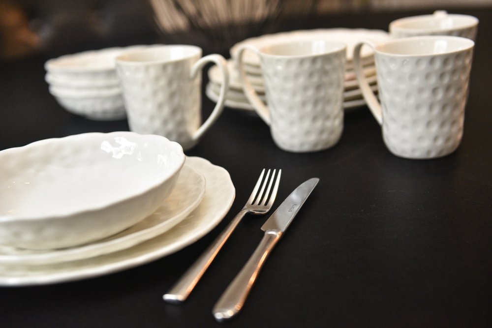 White pebbled porcelain bowls and mugs stacked on a black surface with silverware.
