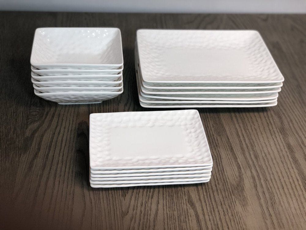 Stack of six white pebbled porcelain bowls on a dark wood surface.