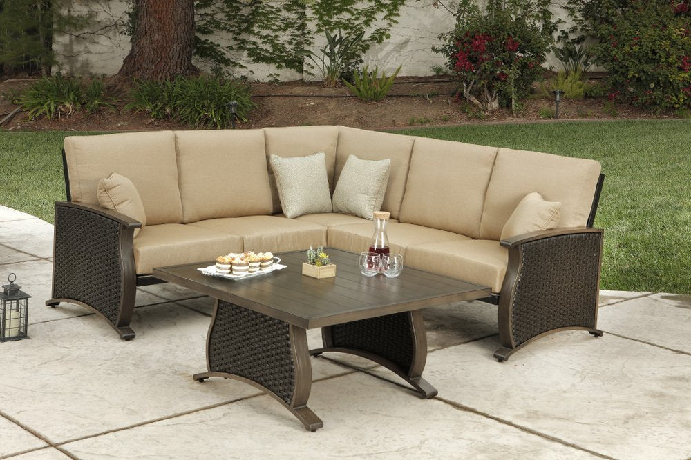 Brown metal sectional sofa with tan cushions and a matching coffee table on a patio with a grassy backyard.