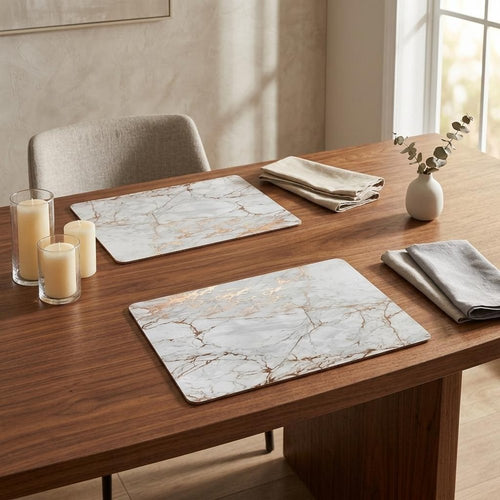 Two marble-patterned placemats with gold and silver veining on a wooden table with candles and napkins.