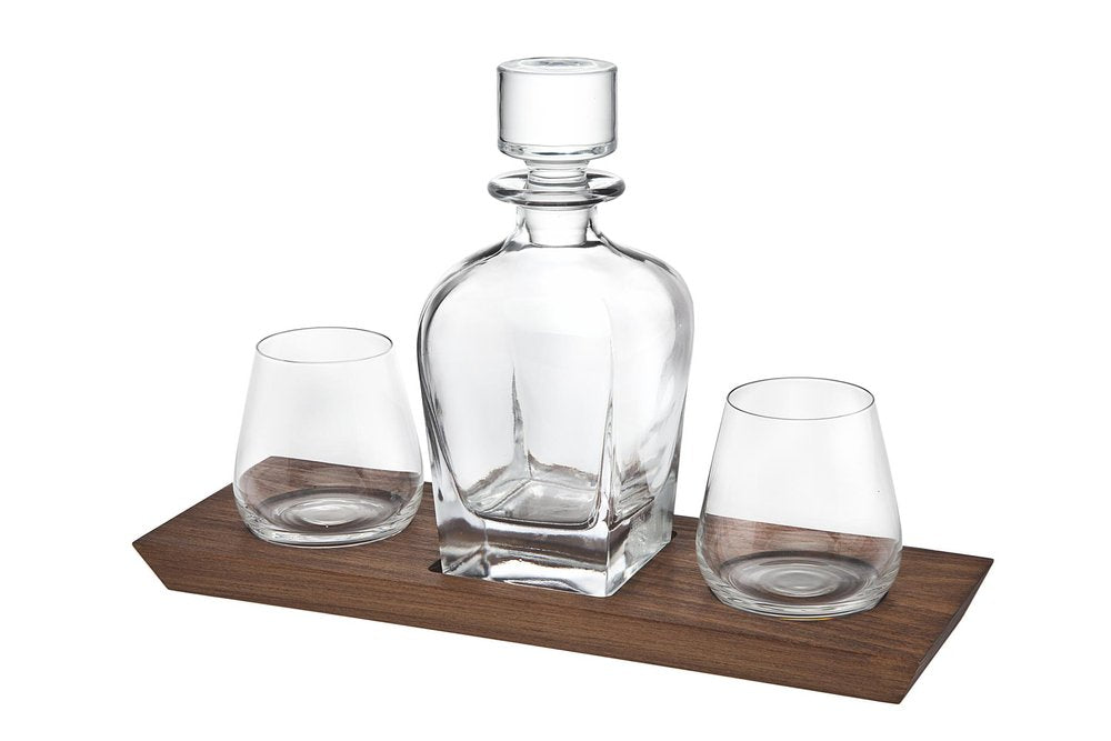 Clear crystal whiskey decanter and two stemless glasses on a dark wood tray.