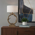 27" Brown Rustic Faux Antlers Table Lamp With White Drum Shade displayed on a dark wood tabletop in a furnished interior against a gray wall.